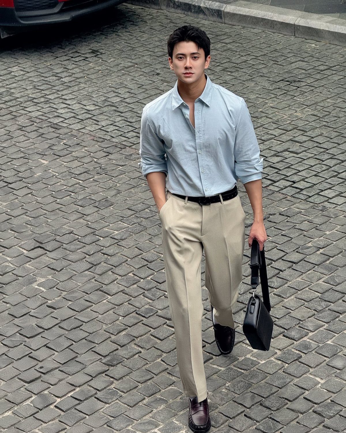 Man in light blue button-down shirt and beige trousers walking on cobblestone street