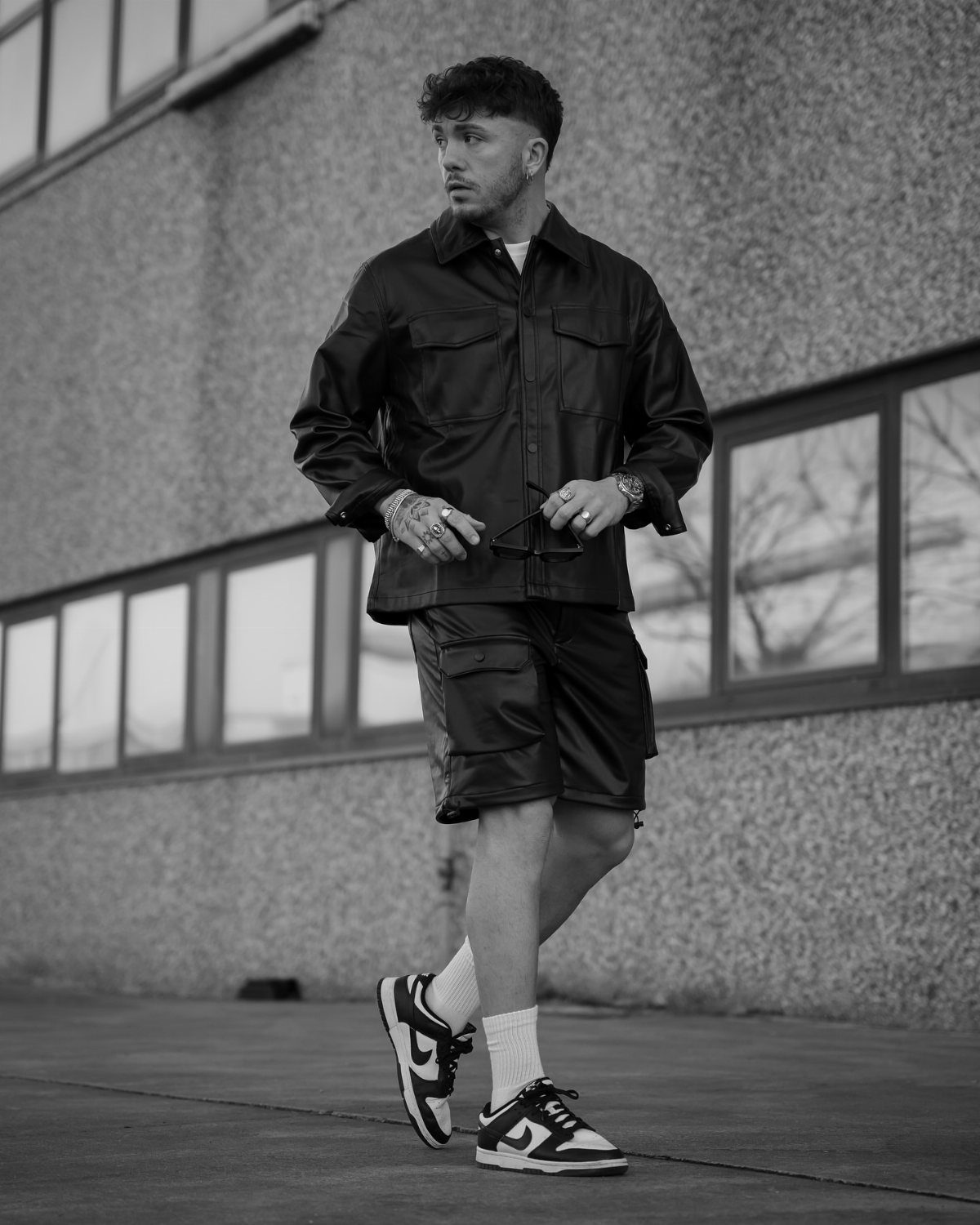 Man wearing a dark jacket, shorts, white socks, and sneakers standing outdoors.