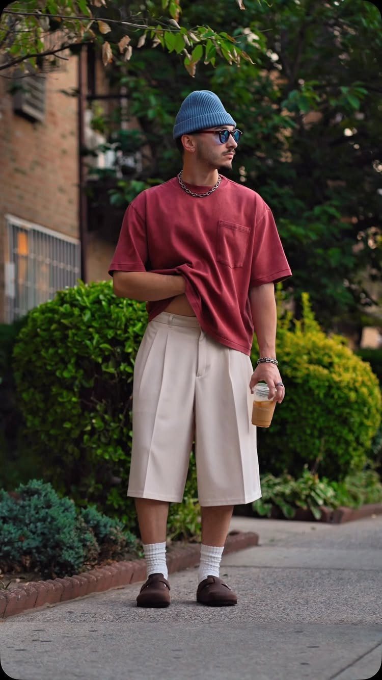 Man in red t-shirt and cream wide-leg shorts wearing a blue beanie outdoors.