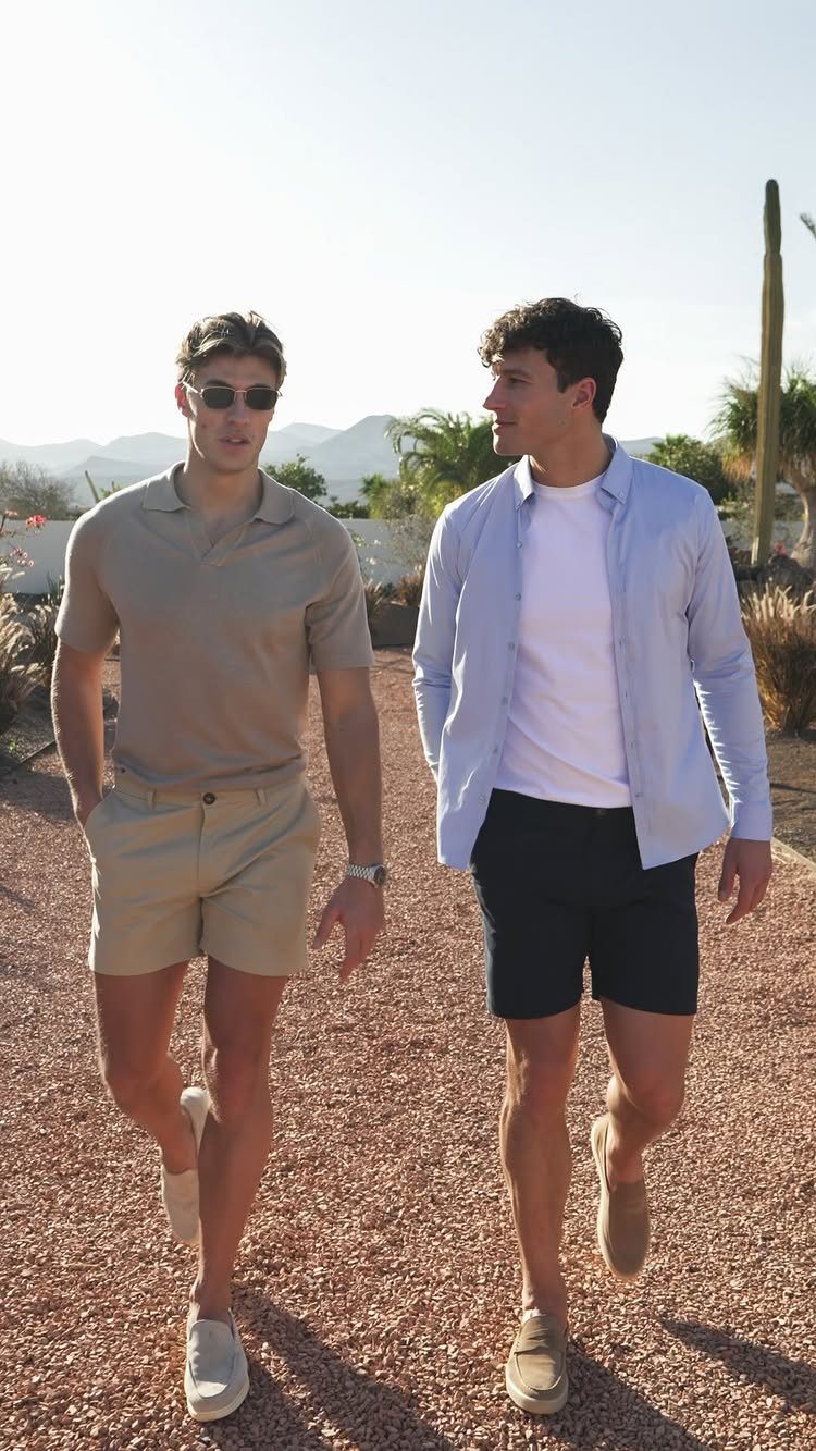 Two men wearing polo shirts and chino shorts walking on a gravel path.