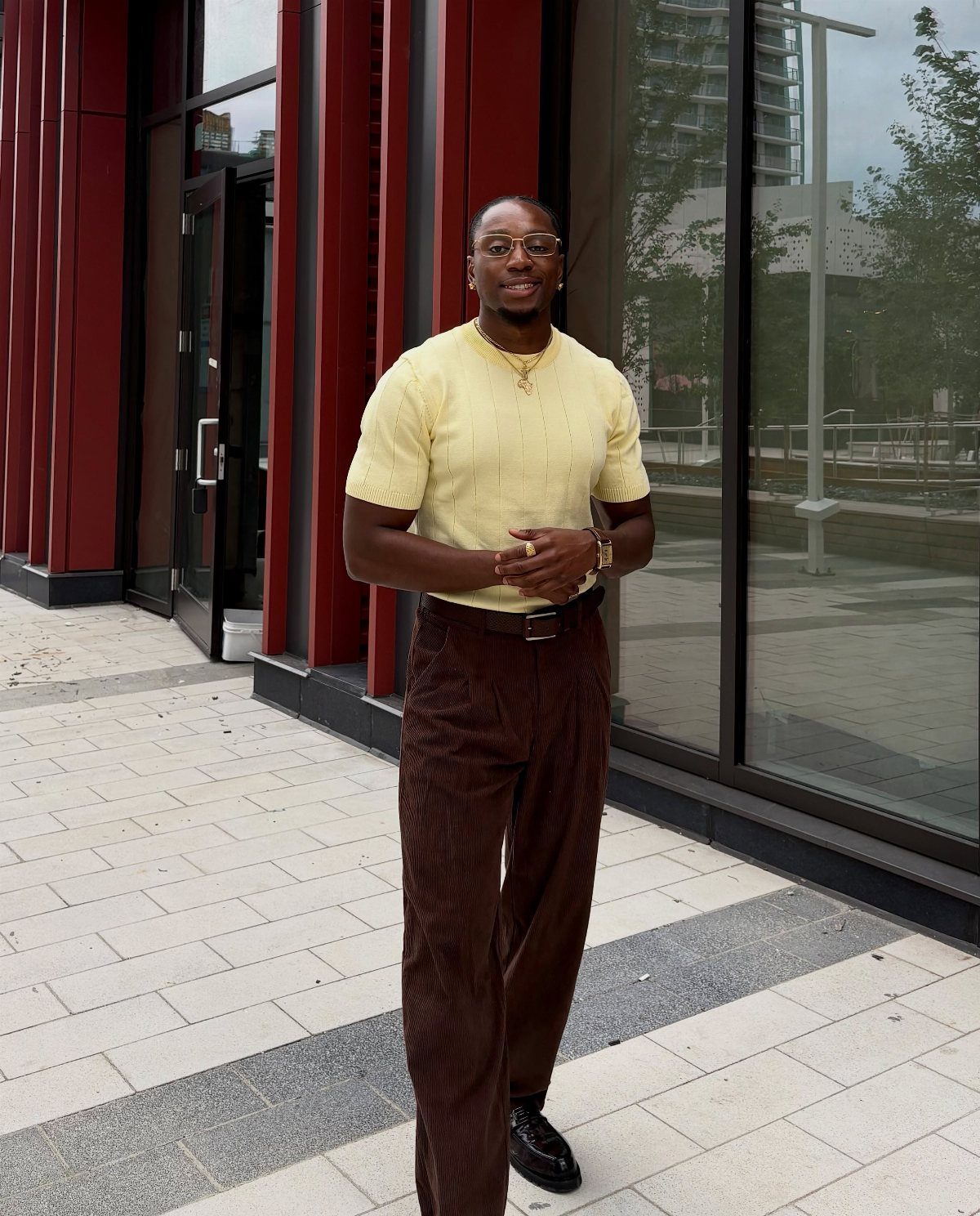 Man wearing a yellow short-sleeved knit shirt and brown patterned trousers outdoors.