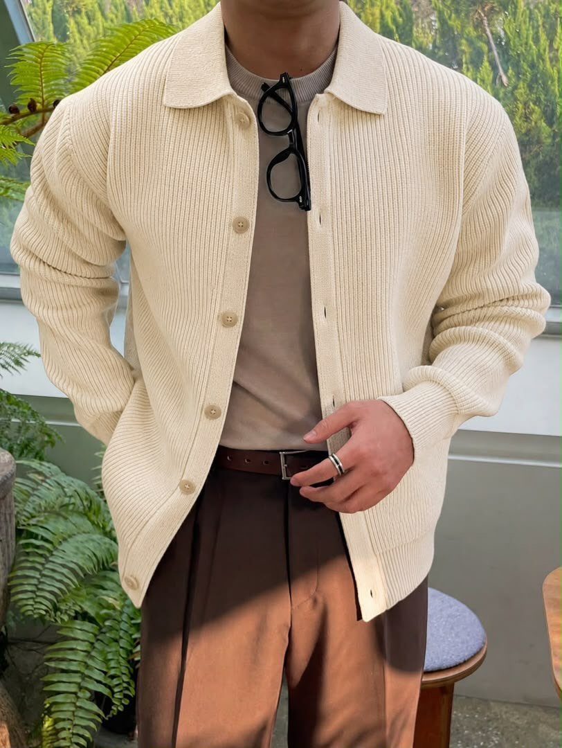 Person wearing a cream ribbed cardigan over a taupe shirt and brown trousers.