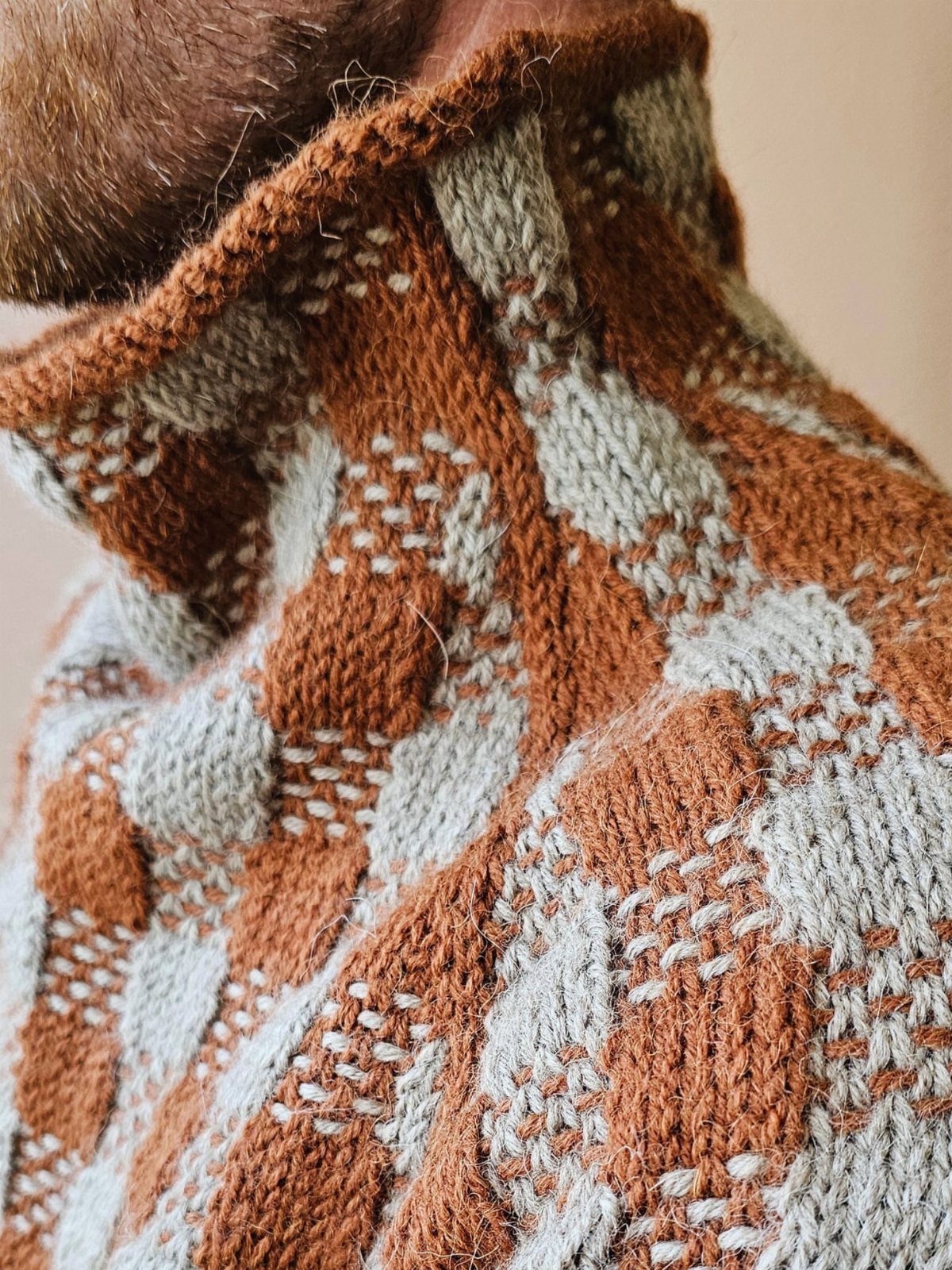Textured knit sweater with rust-orange and grey patterns and a high collar.
