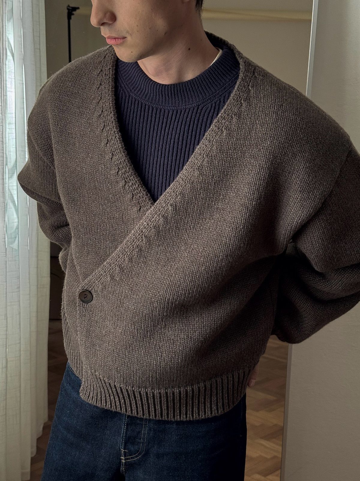 Person wearing a brown knit wrap cardigan, blue ribbed sweater, and dark jeans.