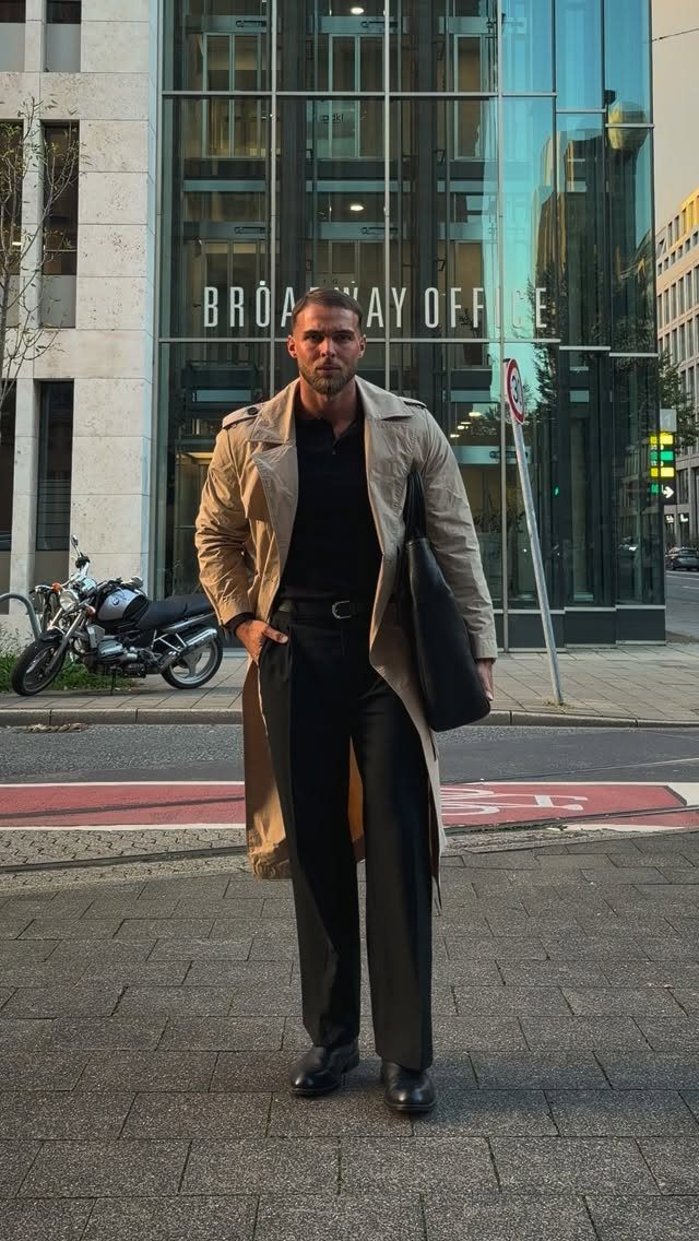 Man in a long beige trench coat and black trousers on a city street.
