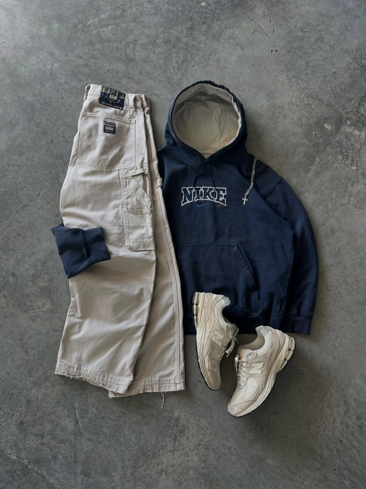 Beige cargo work pants, navy Nike hoodie, and cream sneakers on concrete floor.