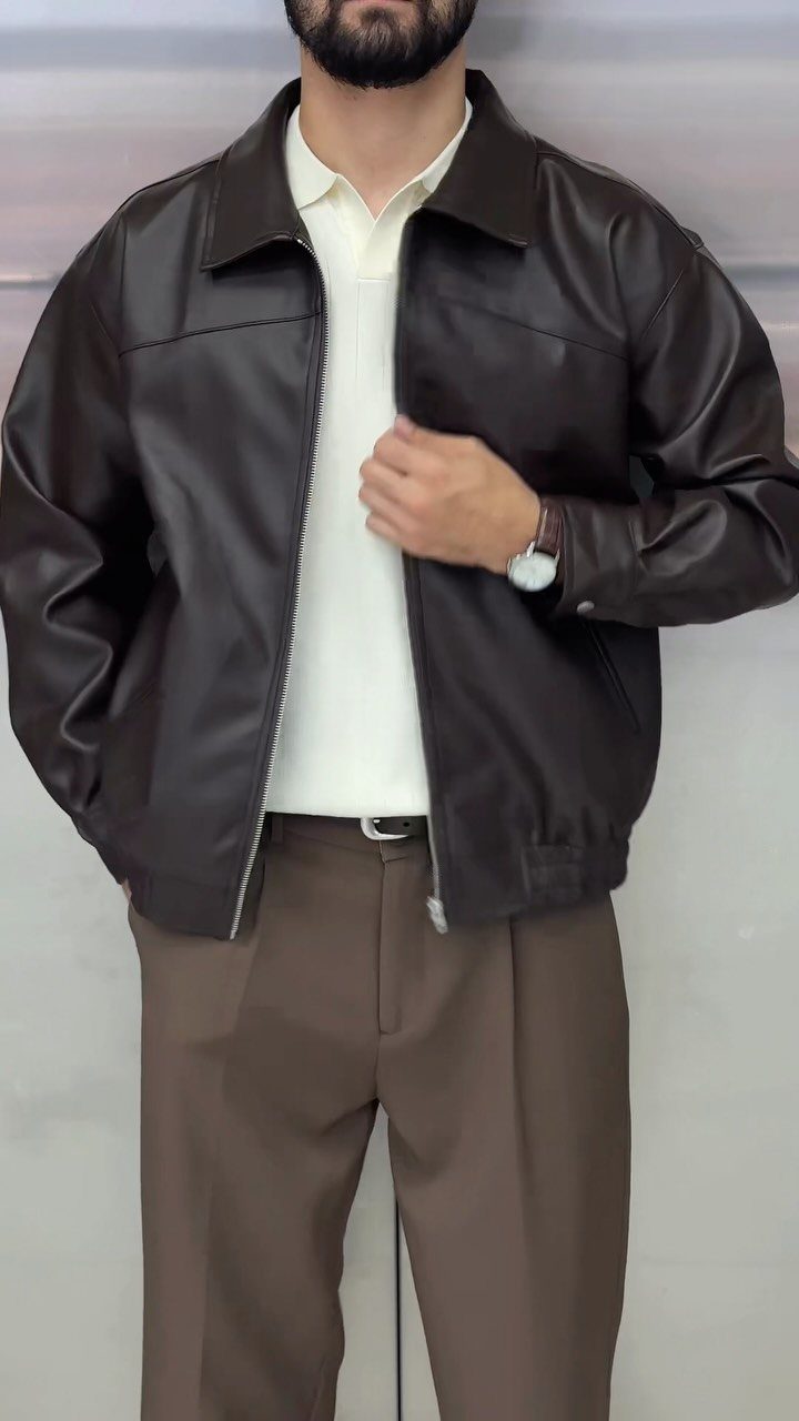 Man wearing a dark brown leather jacket, cream polo, and brown pleated trousers.