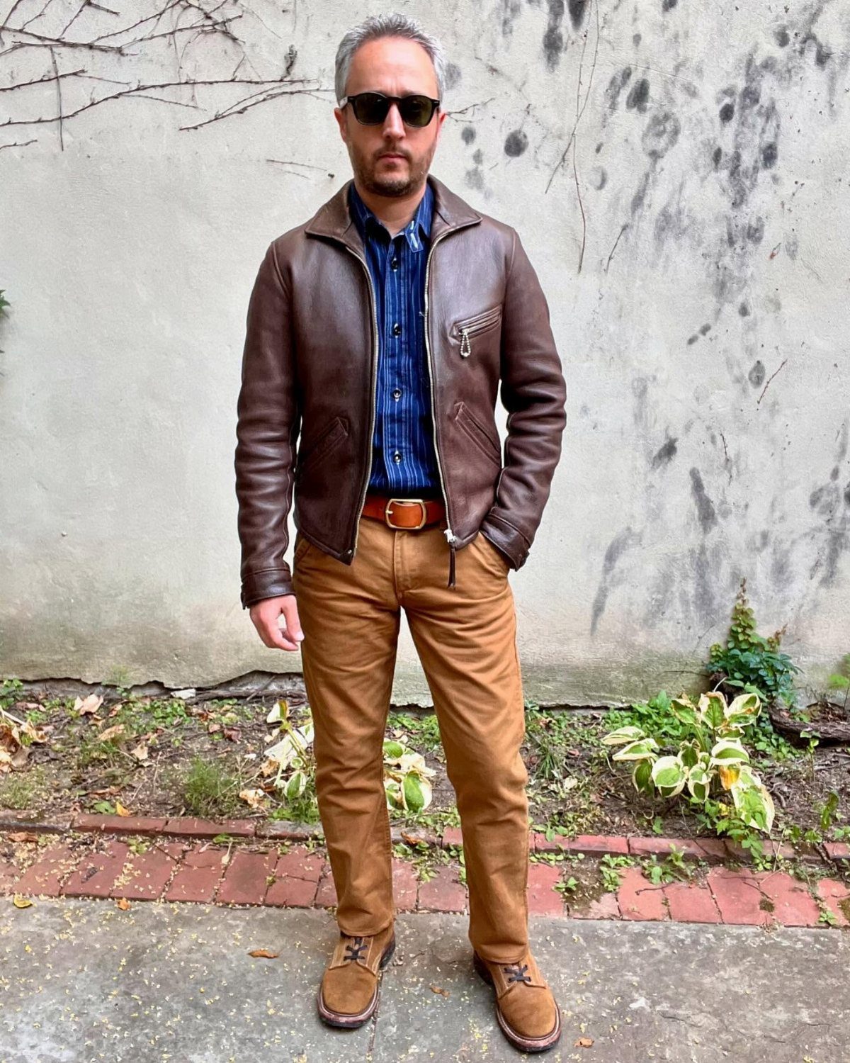 Man wearing a brown leather jacket with tan chinos and a blue shirt.
