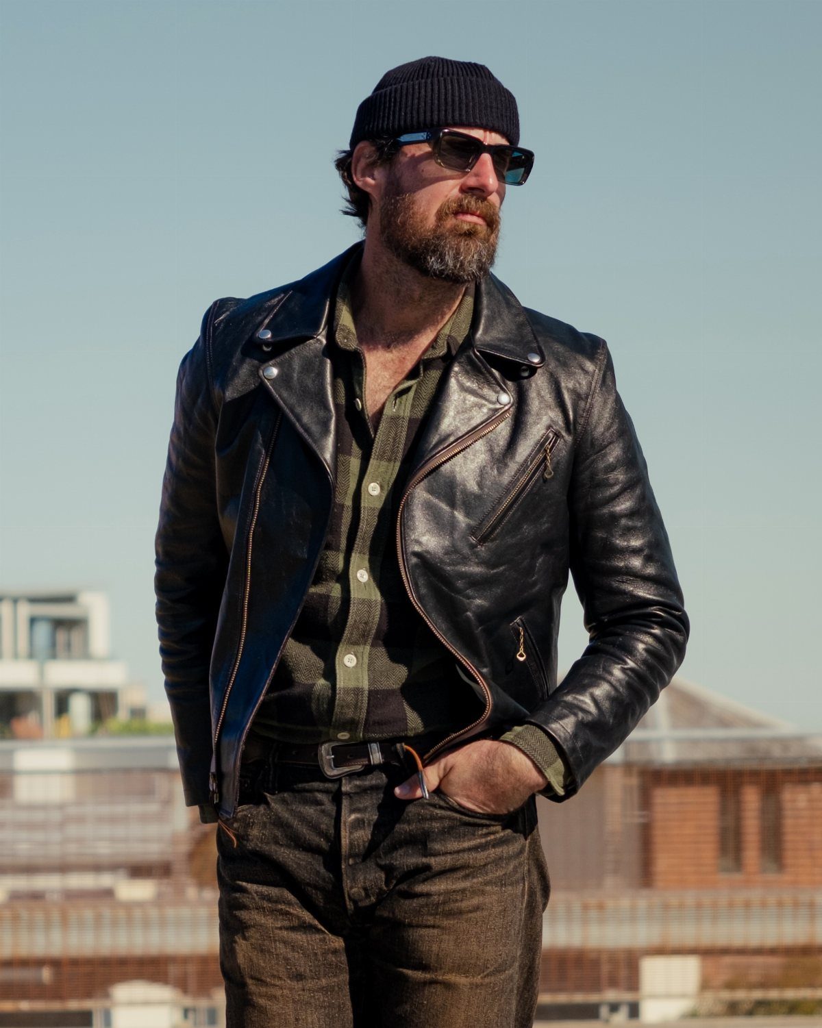 Man wearing a black leather biker jacket over a green plaid flannel shirt