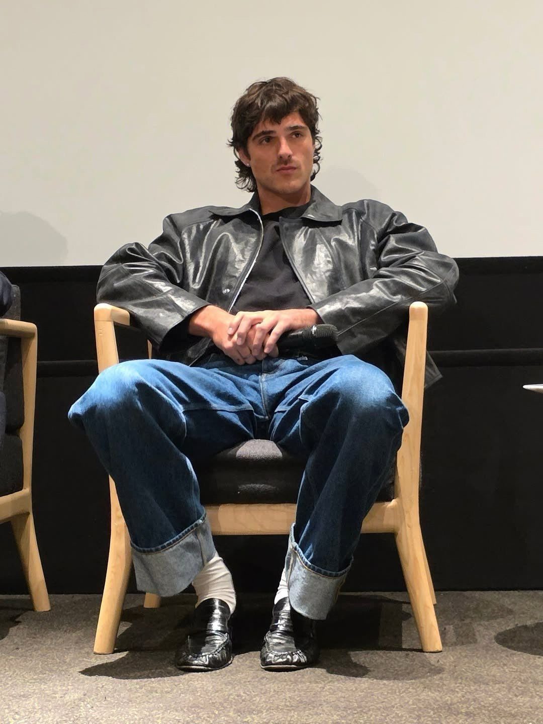 Man wearing an oversized black leather jacket, black t-shirt, and cuffed blue jeans.