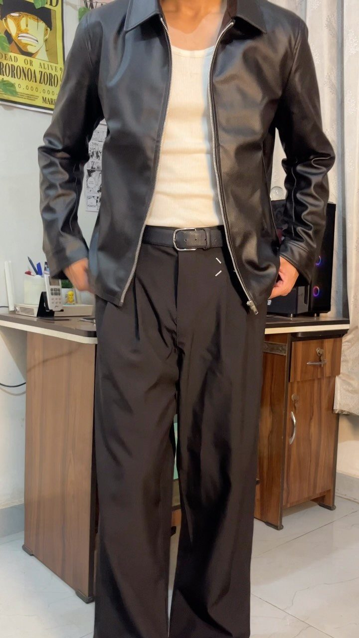 Person wearing a black leather jacket, white tank top, and black wide-leg trousers.