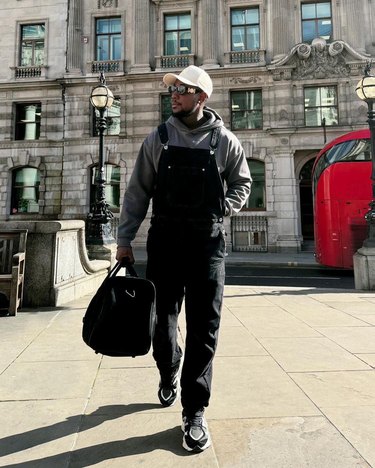 Man wearing black baggy overalls and a grey hoodie walking in a city