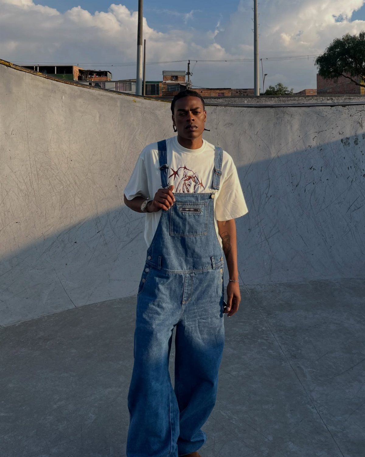 Man wearing baggy blue denim overalls and a white t-shirt in a skate park