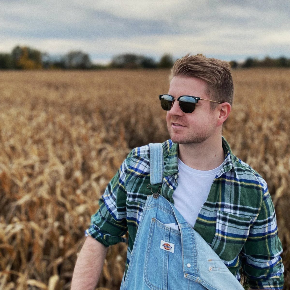 Man in green plaid flannel shirt and blue denim baggy overalls in cornfield