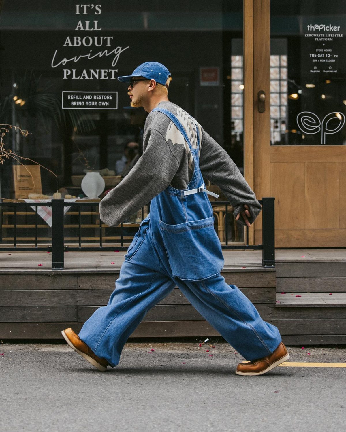 Person walking in wide-leg blue denim overalls, grey shirt, and blue baseball cap.