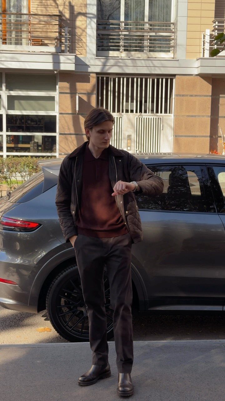 Man wearing a brown Barbour jacket, burgundy sweater, and dark leather Chelsea boots.