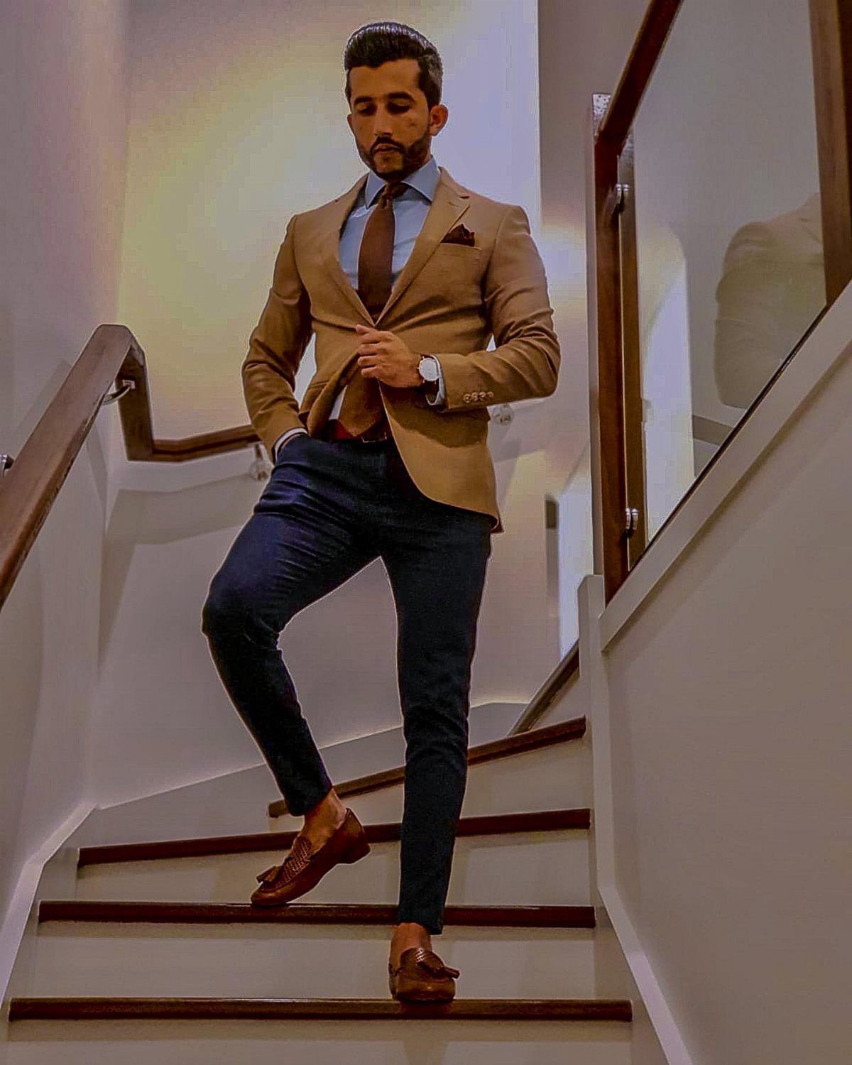 Man in beige blazer and navy chinos posing on a white staircase