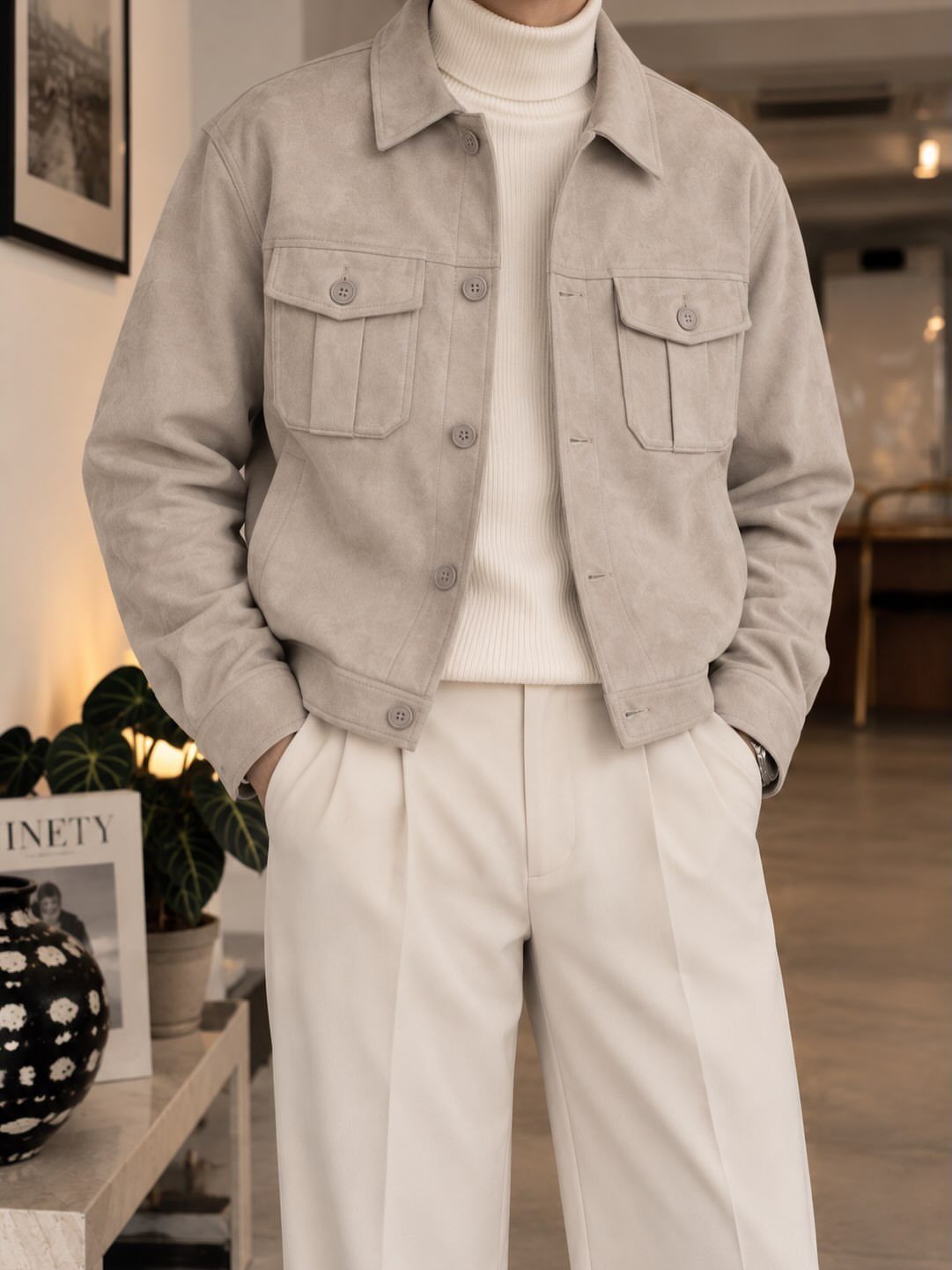 Beige suede jacket worn with a white turtleneck and white pleated trousers.