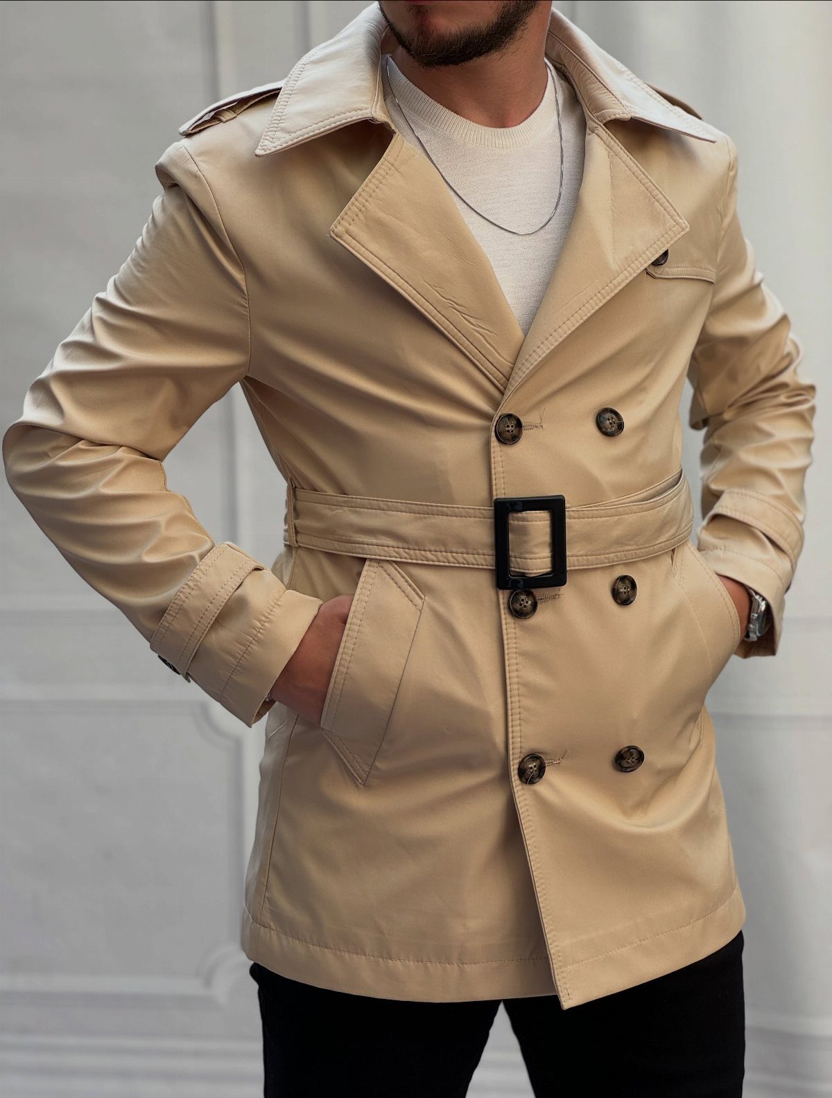 Beige double-breasted trench coat featuring dark brown horn buttons and a belted waist.
