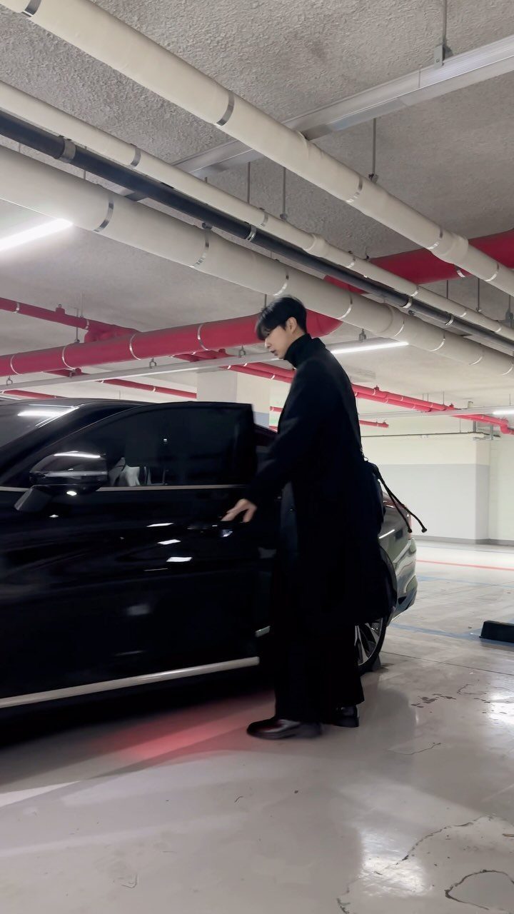 Man in long black coat and black leather shoes standing by black car
