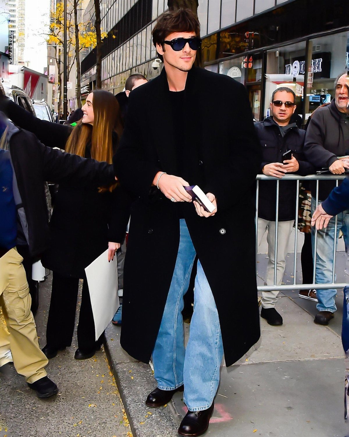 Man in a long black coat and light blue jeans walking on city street