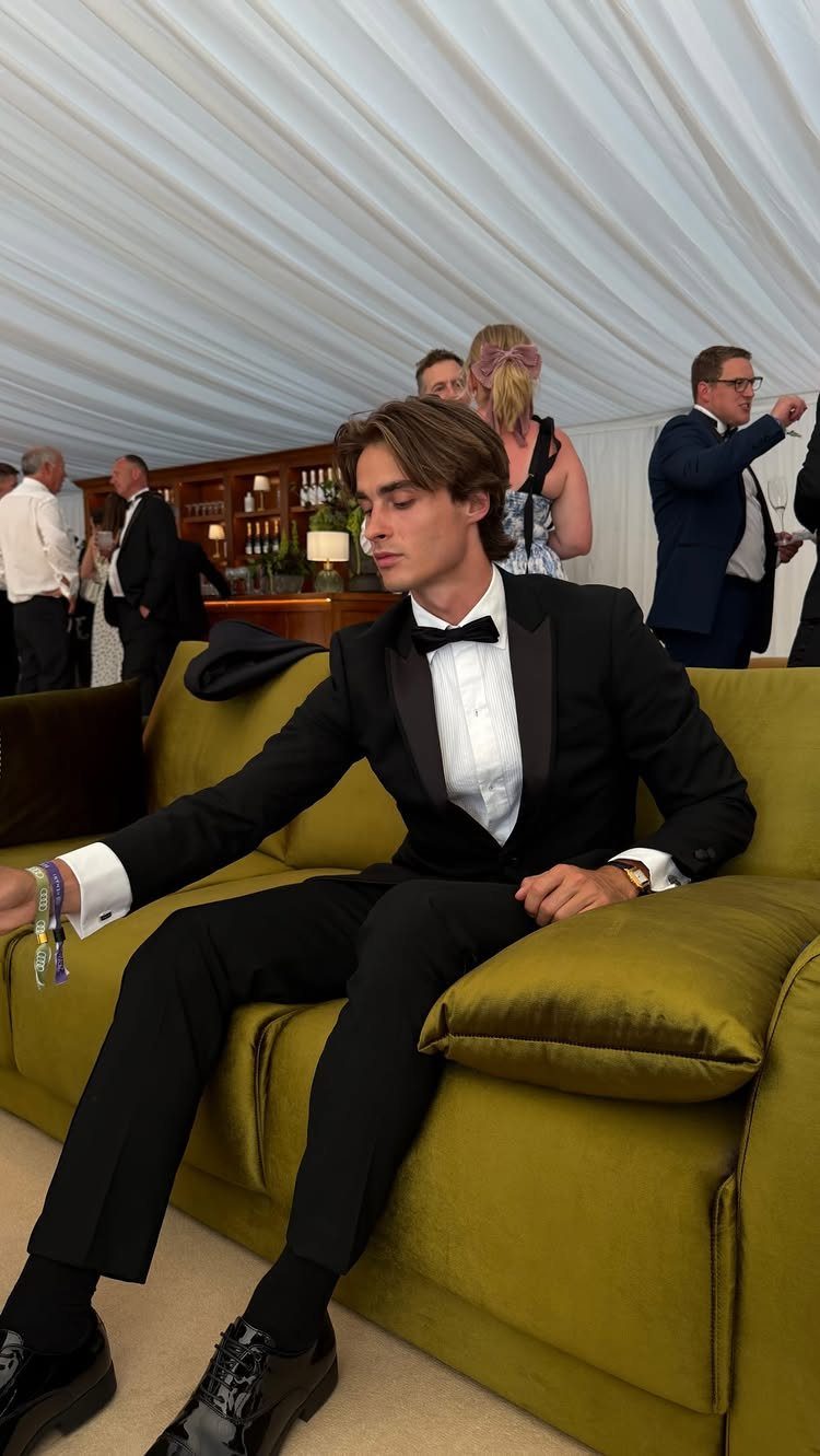 Man in a black tuxedo and bow tie sitting on a yellow velvet sofa