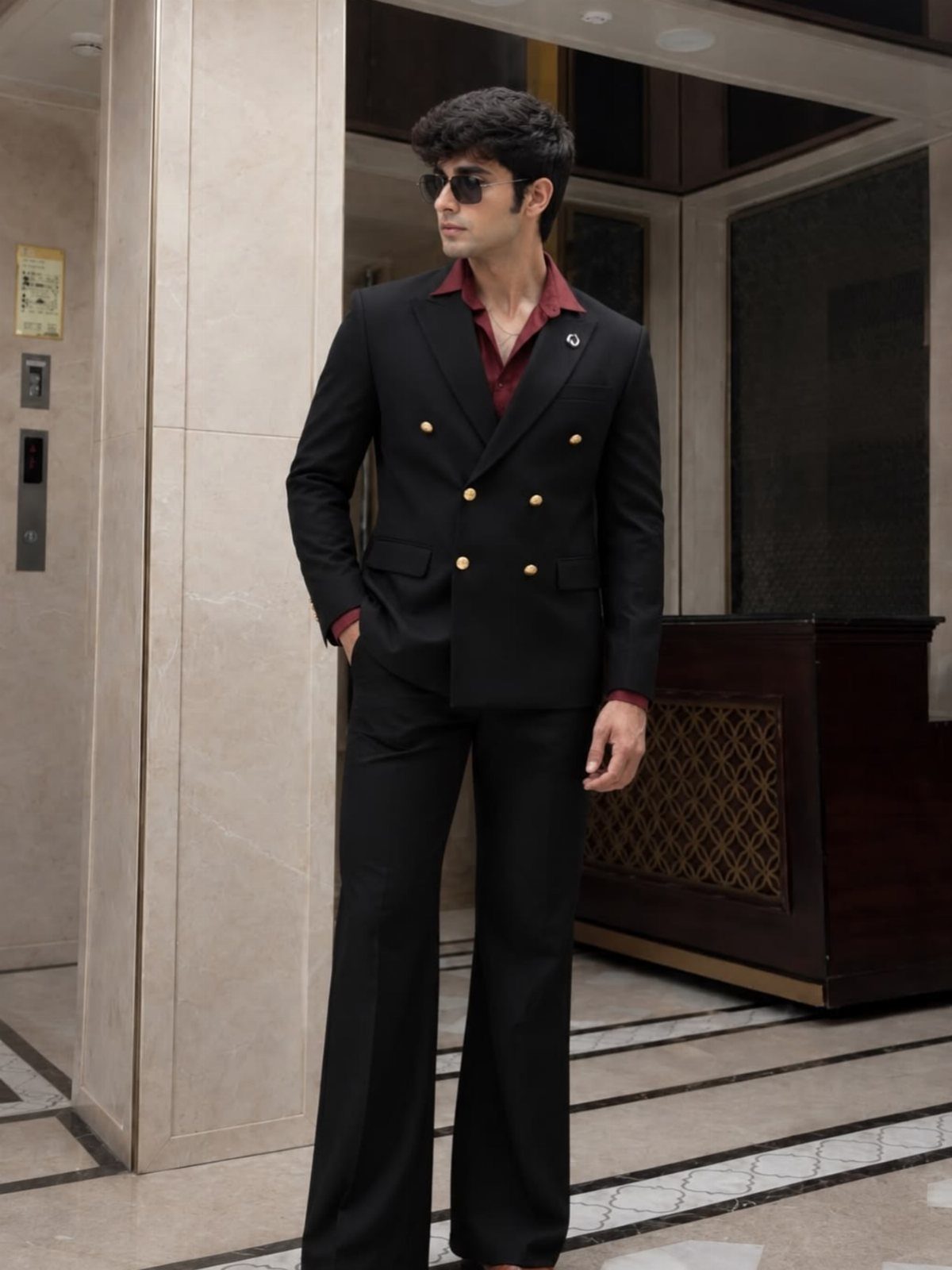 Man in a black double-breasted blazer and wide-leg black trousers in a lobby