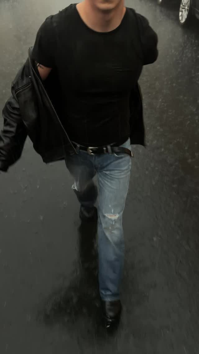 Person wearing a black leather jacket and blue ripped jeans on dark pavement