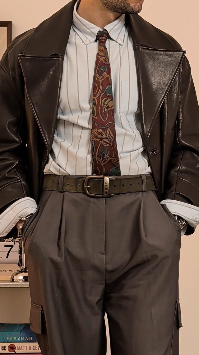 Person wearing a black leather jacket with a pinstriped button-down shirt and tie.