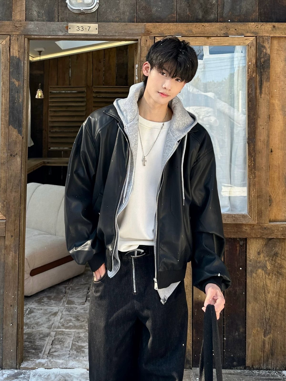 Man wearing a black leather jacket over a grey hoodie and black pants.