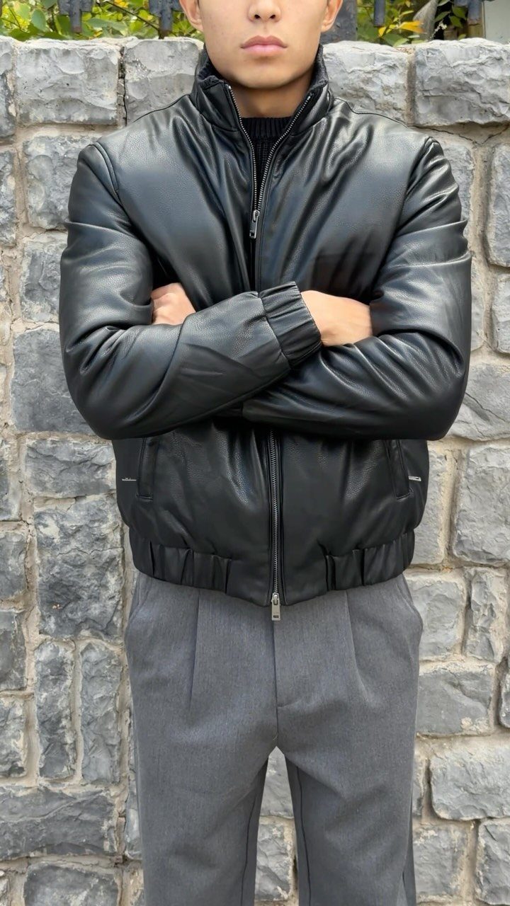 Man wearing a black leather jacket with a black turtleneck and grey trousers.