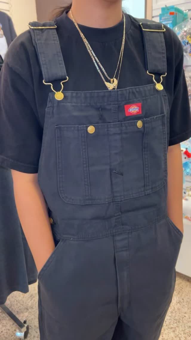 Person wearing black overalls over a black t-shirt with gold necklaces.