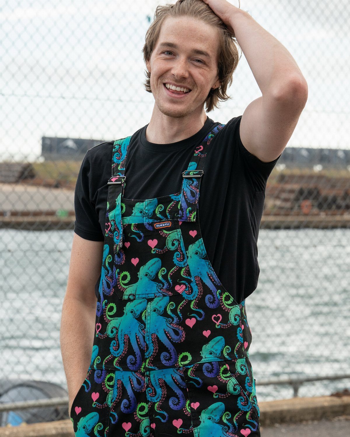 Man wearing black overalls with aquamarine octopus print and a black t-shirt.