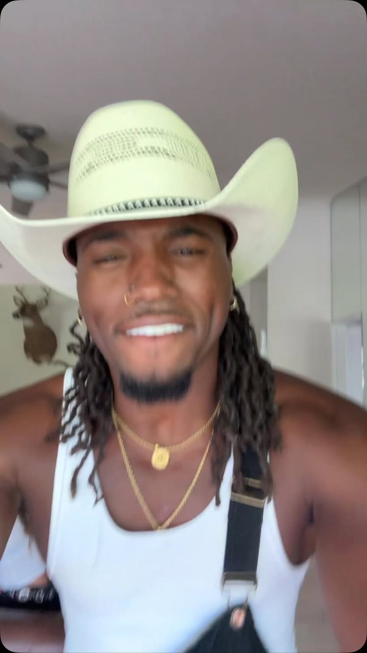 Man in white cowboy hat and tank top wearing black overalls