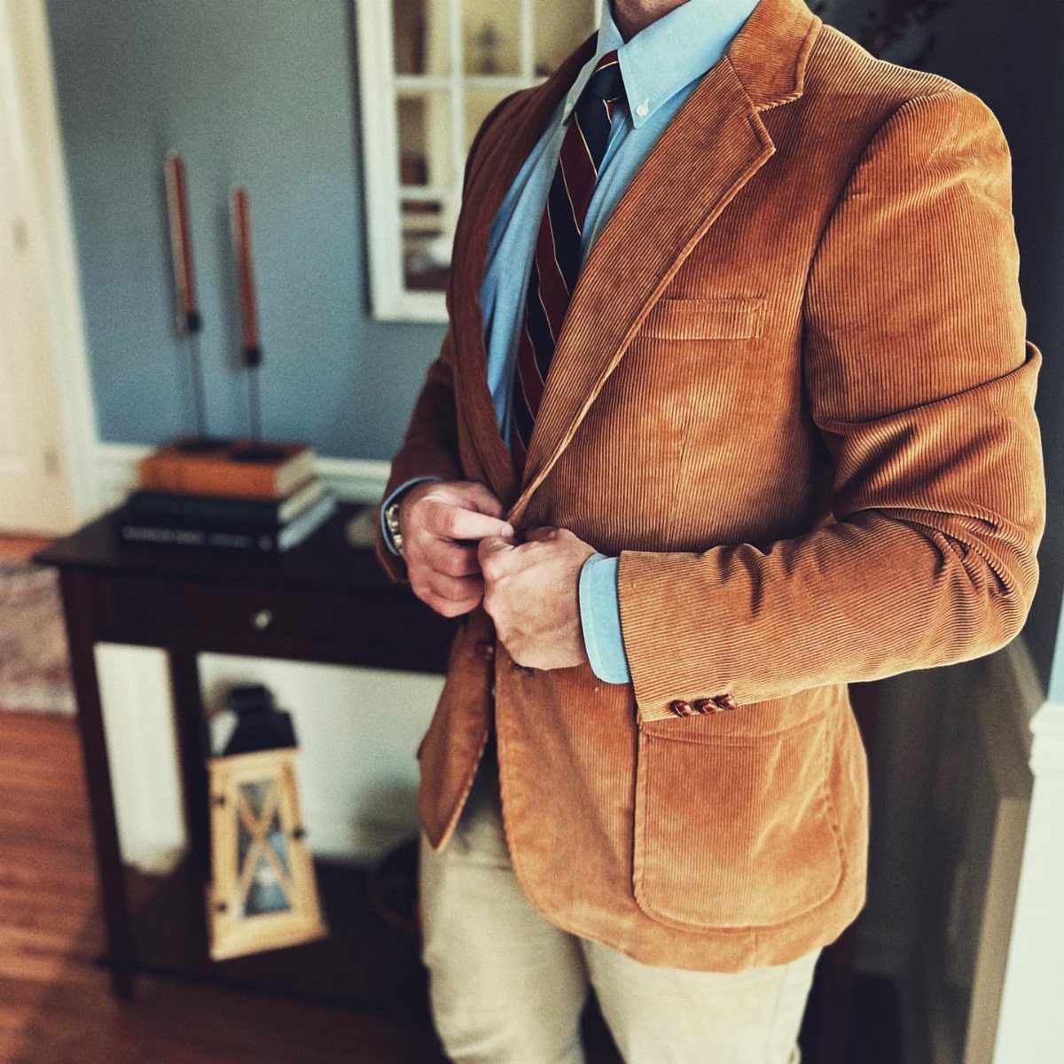 Man wearing a brown corduroy jacket with a blue shirt and khaki chinos.