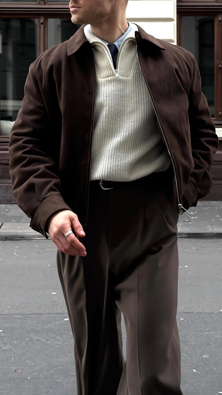 Man wearing a brown jacket, white textured sweater, and matching brown trousers outdoors.