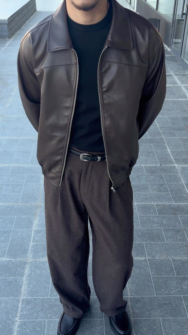 Man wearing a brown leather jacket, black t-shirt, and brown pleated trousers.