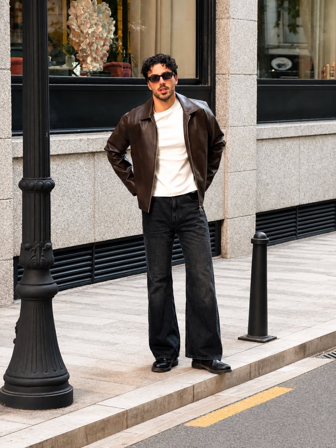 Man wearing a brown leather jacket, white t-shirt, and wide-leg black jeans.