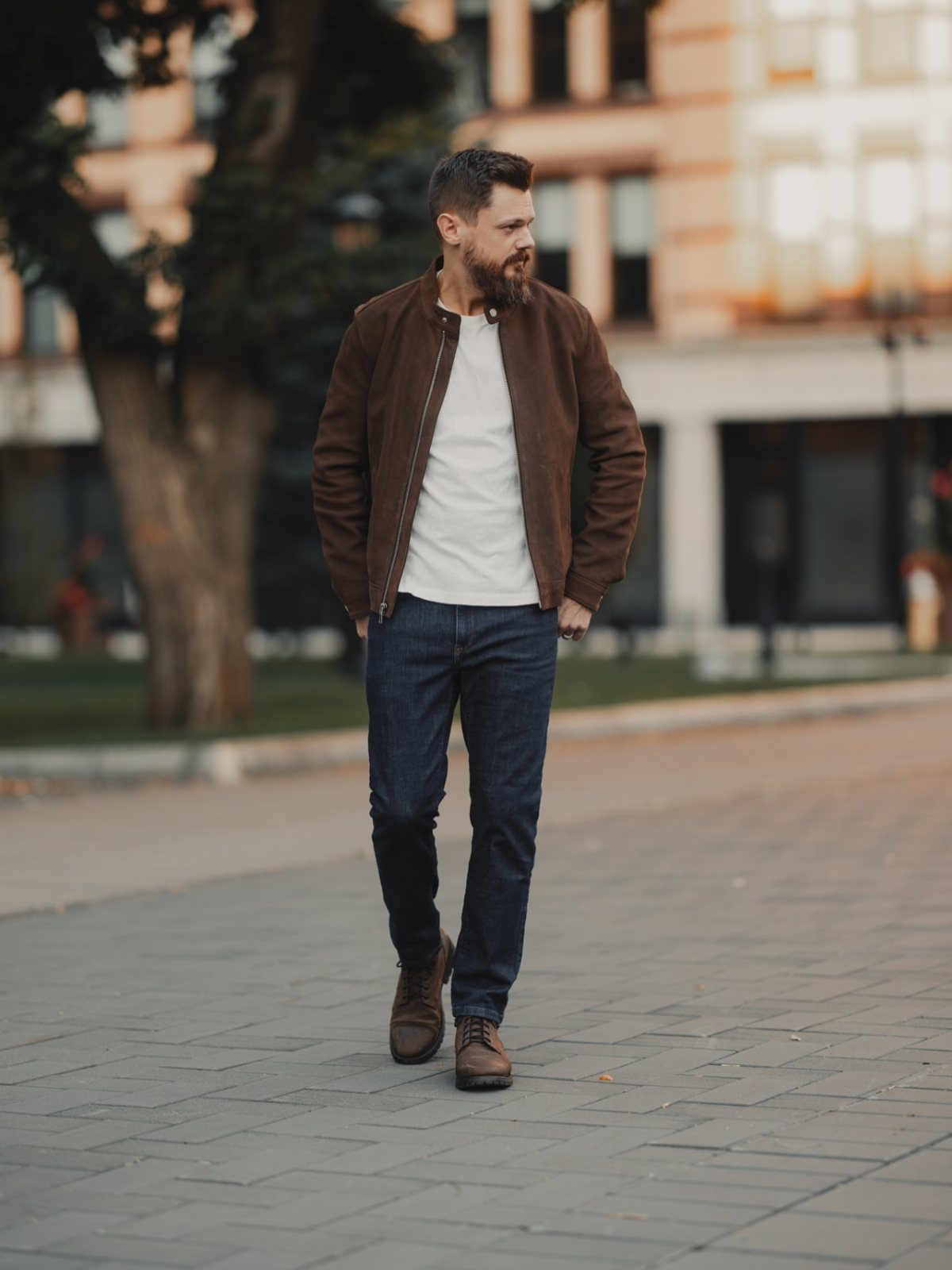 Man wearing a brown bomber jacket, white shirt, navy jeans, and brown boots.