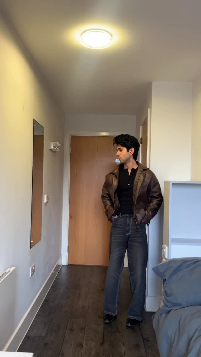 Man wearing a brown leather jacket and dark blue jeans in a hallway