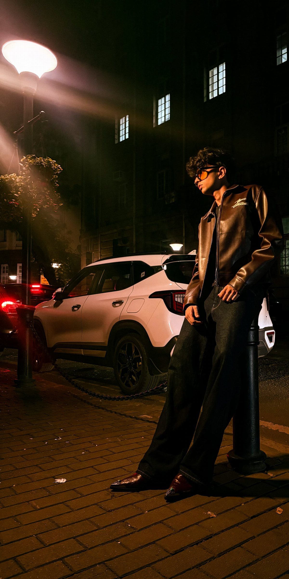 Person wearing a brown leather jacket and dark jeans standing on a city street