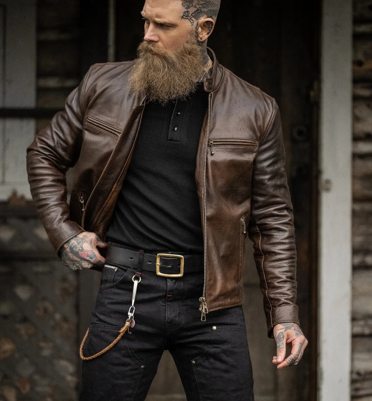 Bearded man wearing a brown leather jacket, black polo shirt, and black jeans.