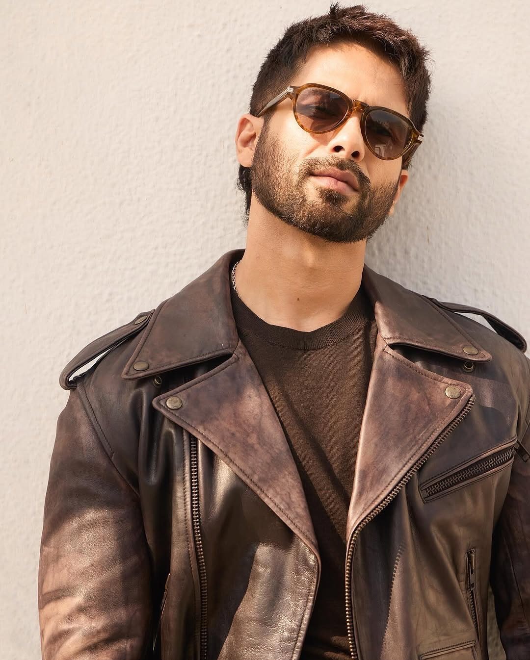 Man wearing a distressed brown leather jacket and brown sweater with sunglasses.