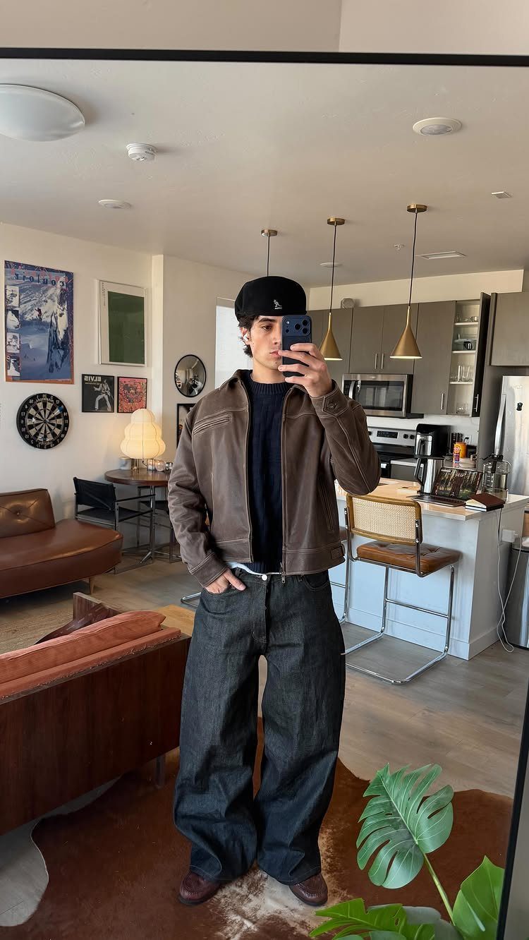 Person wearing a brown leather jacket, black beanie, and wide-leg dark jeans in a room.