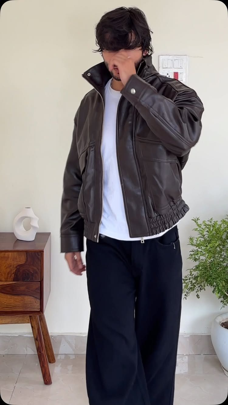 Man wearing a dark brown leather jacket, white t-shirt, and black wide-leg trousers.