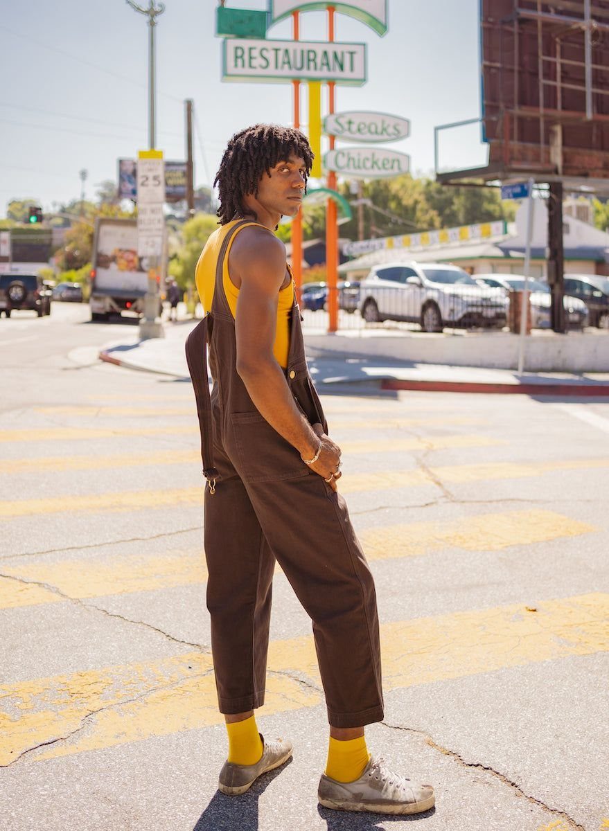 Person wearing brown wide-leg overalls and a yellow sleeveless top on a city street