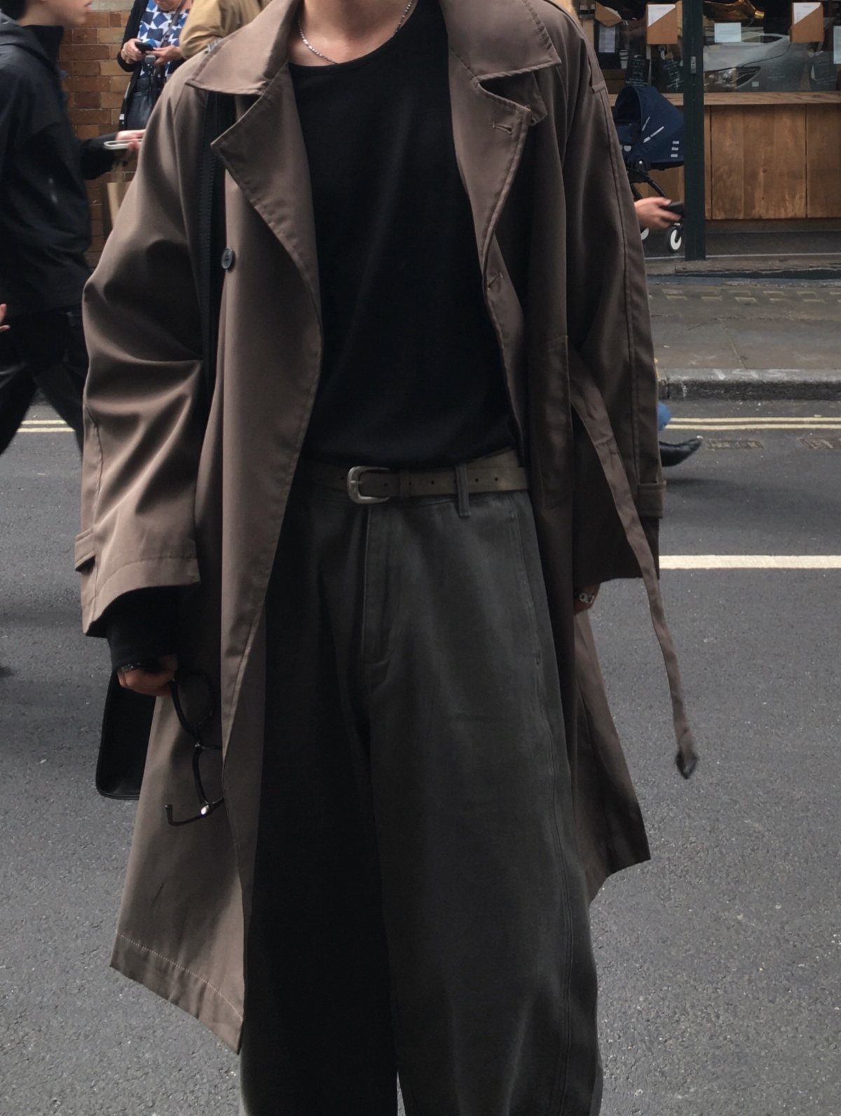 Person wearing a brown trench coat with a black shirt and charcoal trousers.