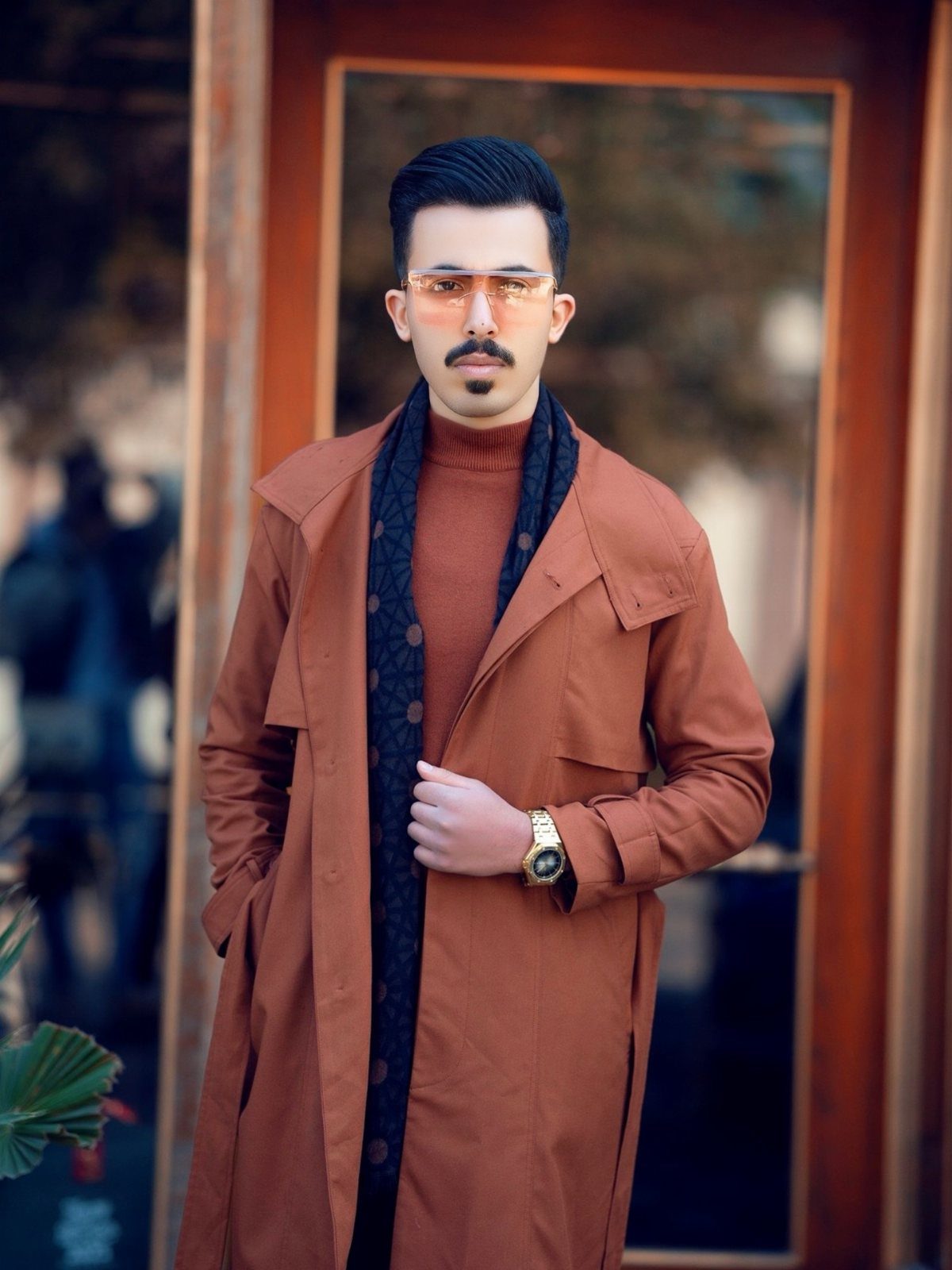 Man in a brown trench coat, brown turtleneck, and dark patterned scarf.