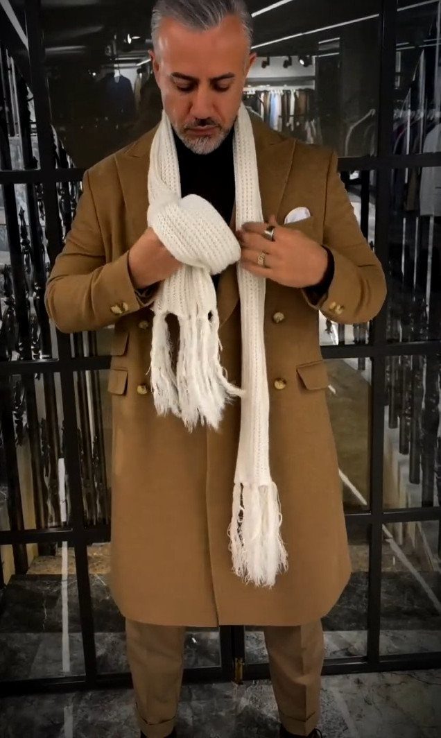 Man in a brown double-breasted coat with a white scarf and tan trousers.