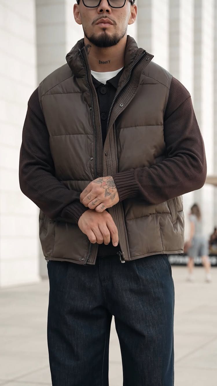Man wearing a brown puffer vest, dark brown shirt, and navy blue jeans.